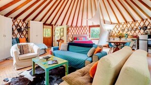 A cozy interior of a yurt with a wooden ceiling, a sofa, a coffee table, and a dining area. - Totally secluded Yurt surrounded by waterfalls, brooks, cliffs and forest (Ulster Park)