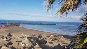 Una playa con sombrillas de paja y una motocicleta estacionada.
