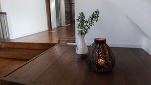 Una escalera de madera que conduce a una habitación con pared blanca, un jarrón blanco con follaje verde y un farol negro con detalles anaranjados.