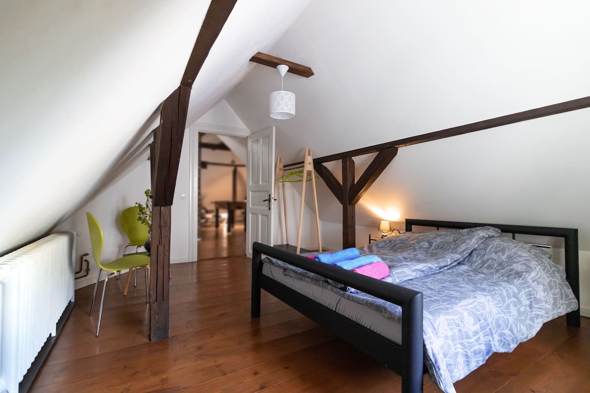 Un dormitorio con techo inclinado, una cama con colcha estampada, una silla verde y un radiador.