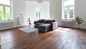 Amplia sala de estar con piso de madera, un sofá modular gris, una mesita de noche blanca y un jarrón con flores.