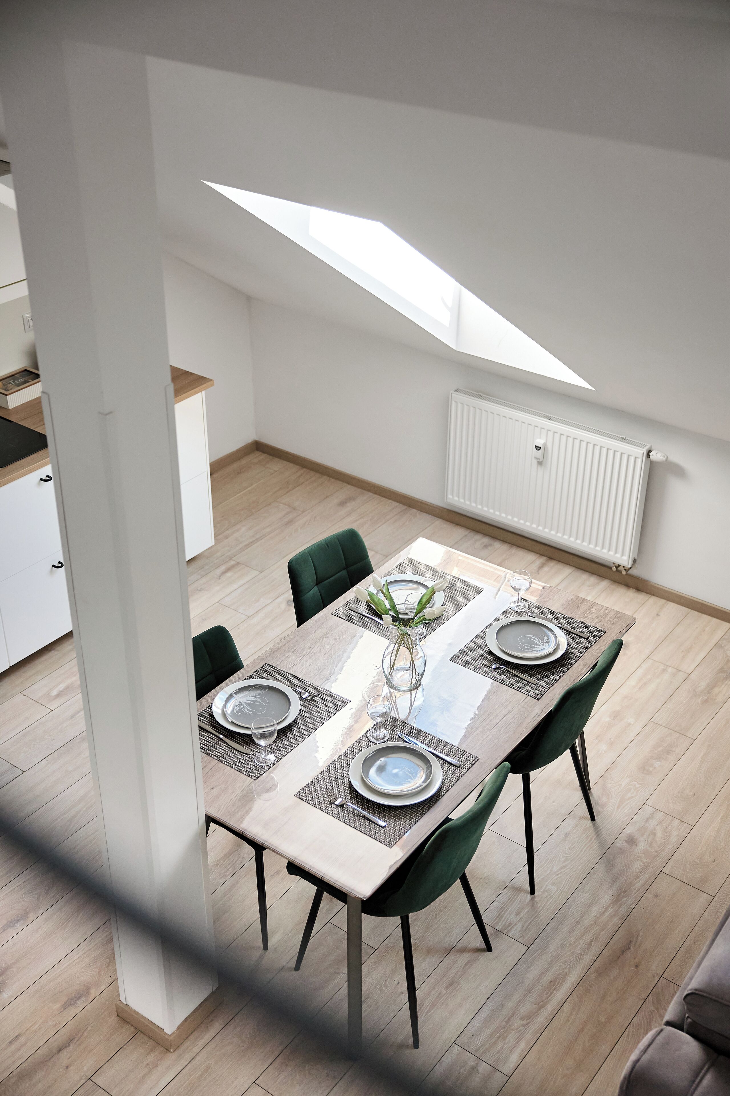 A dining area with a table set for four, green chairs, and a skylight above.