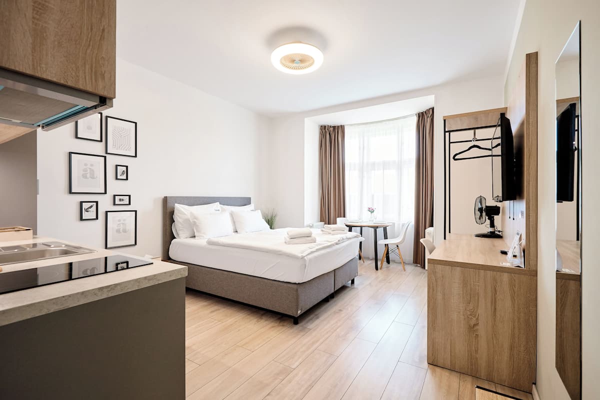 Una habitación de hotel moderna con una cama, una pequeña mesa de comedor, una zona de cocina y un televisor.