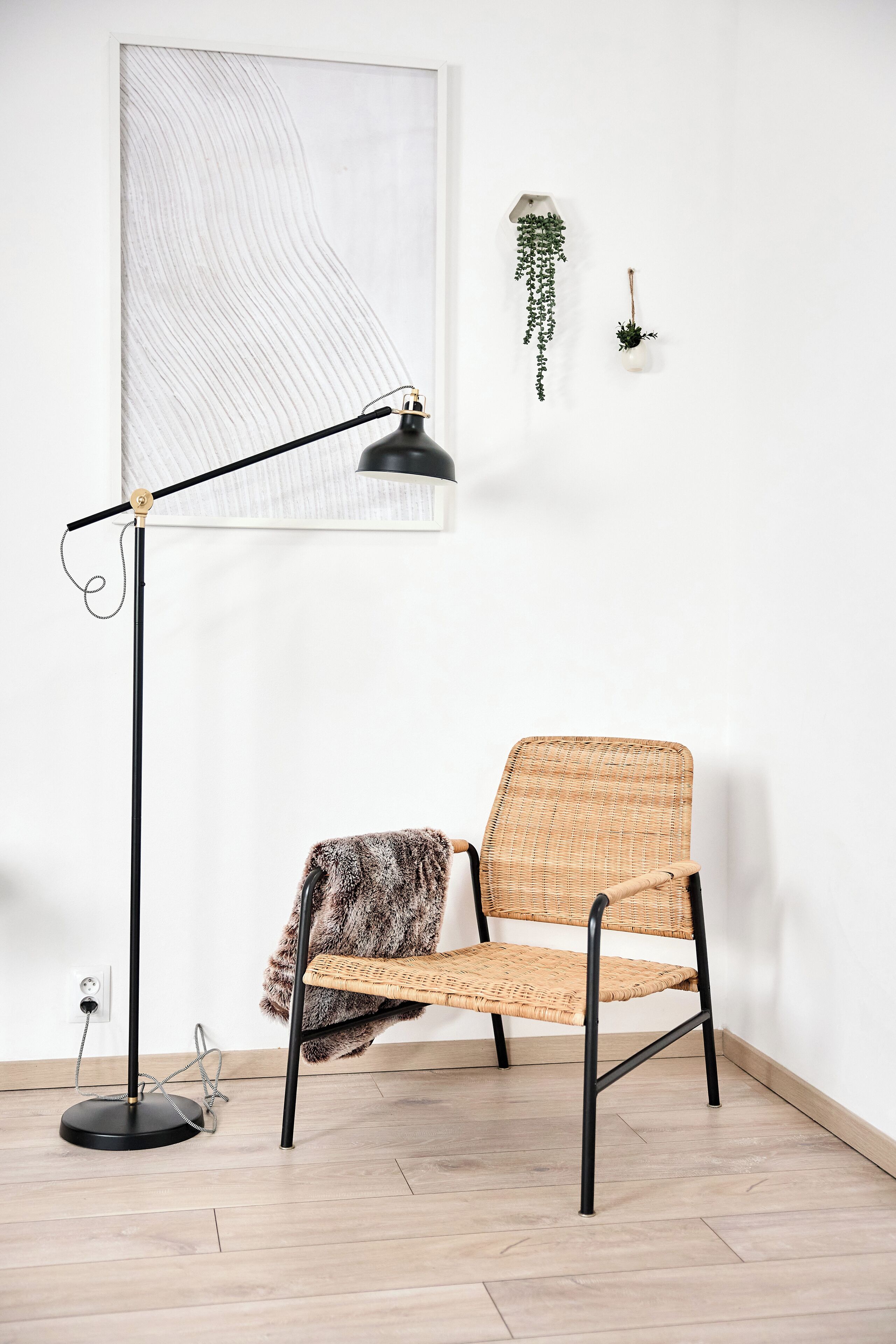 A room with a modern chair, a floor lamp, and a hanging plant.