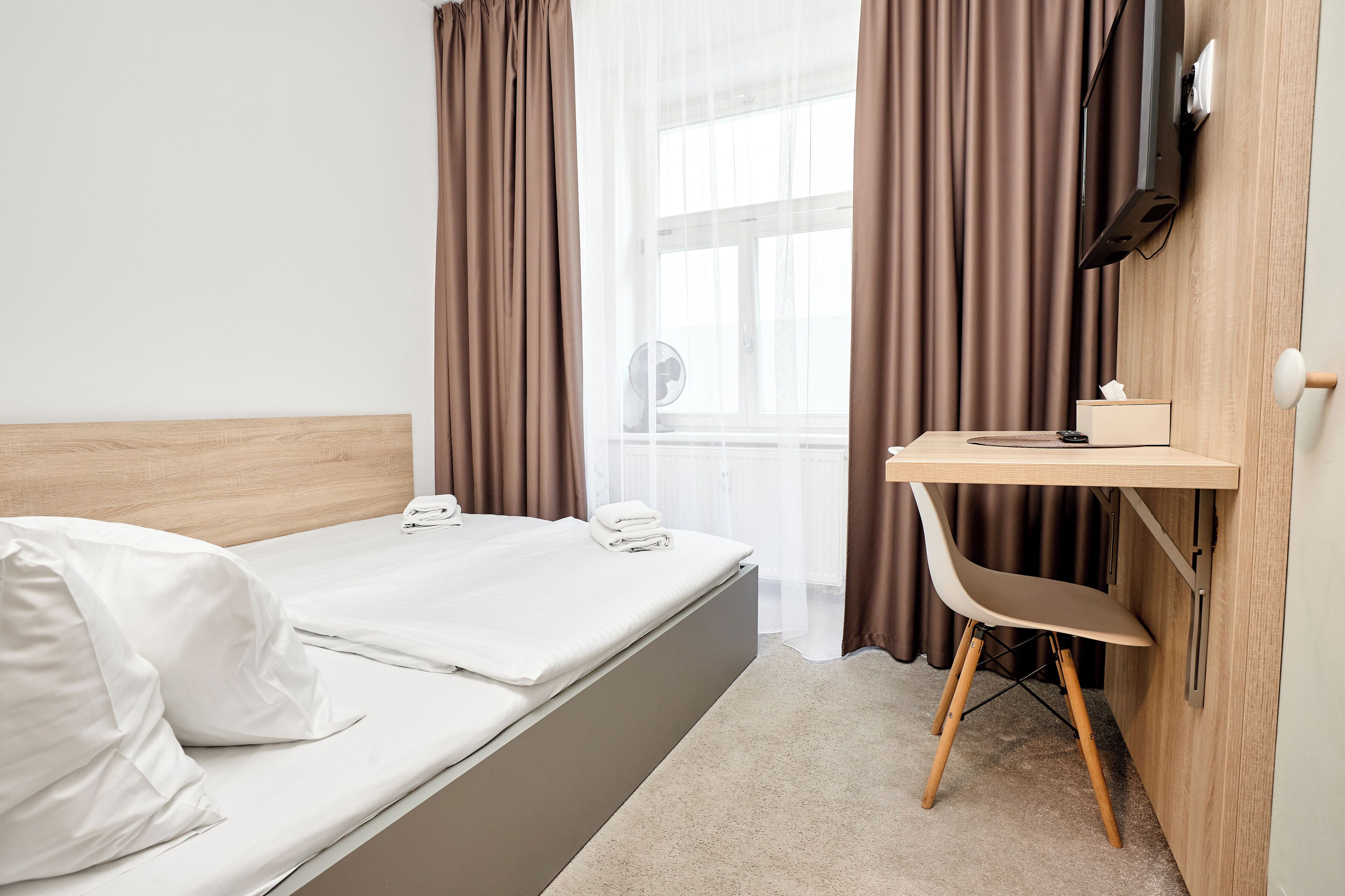 Habitación de hotel con cama, escritorio, silla, televisor y ventana con cortinas.