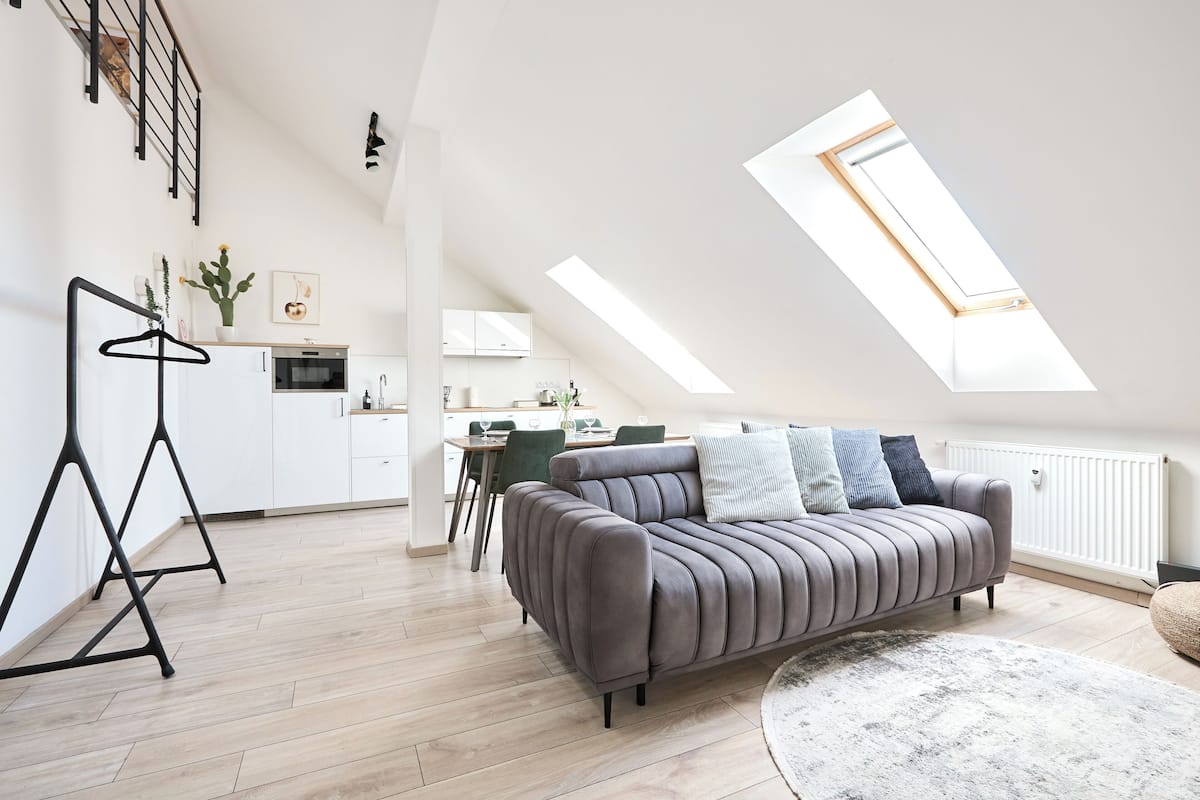 Un loft moderno con comedor, cocina y un sofá gris con almohadones.