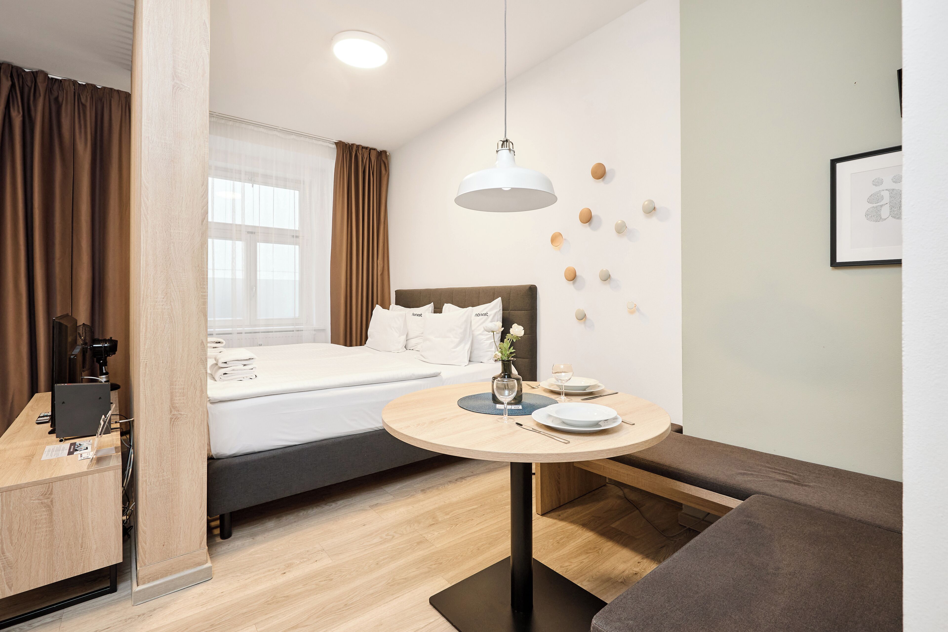 Una habitación de hotel con una cama, un escritorio, una mesa redonda con platos y vasos, y una lámpara fijada a la pared.