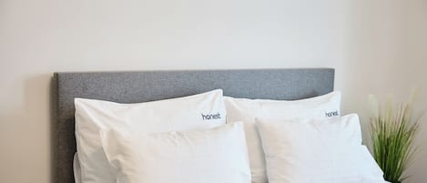 Una cama con cabecera gris y ropa de cama blanca.