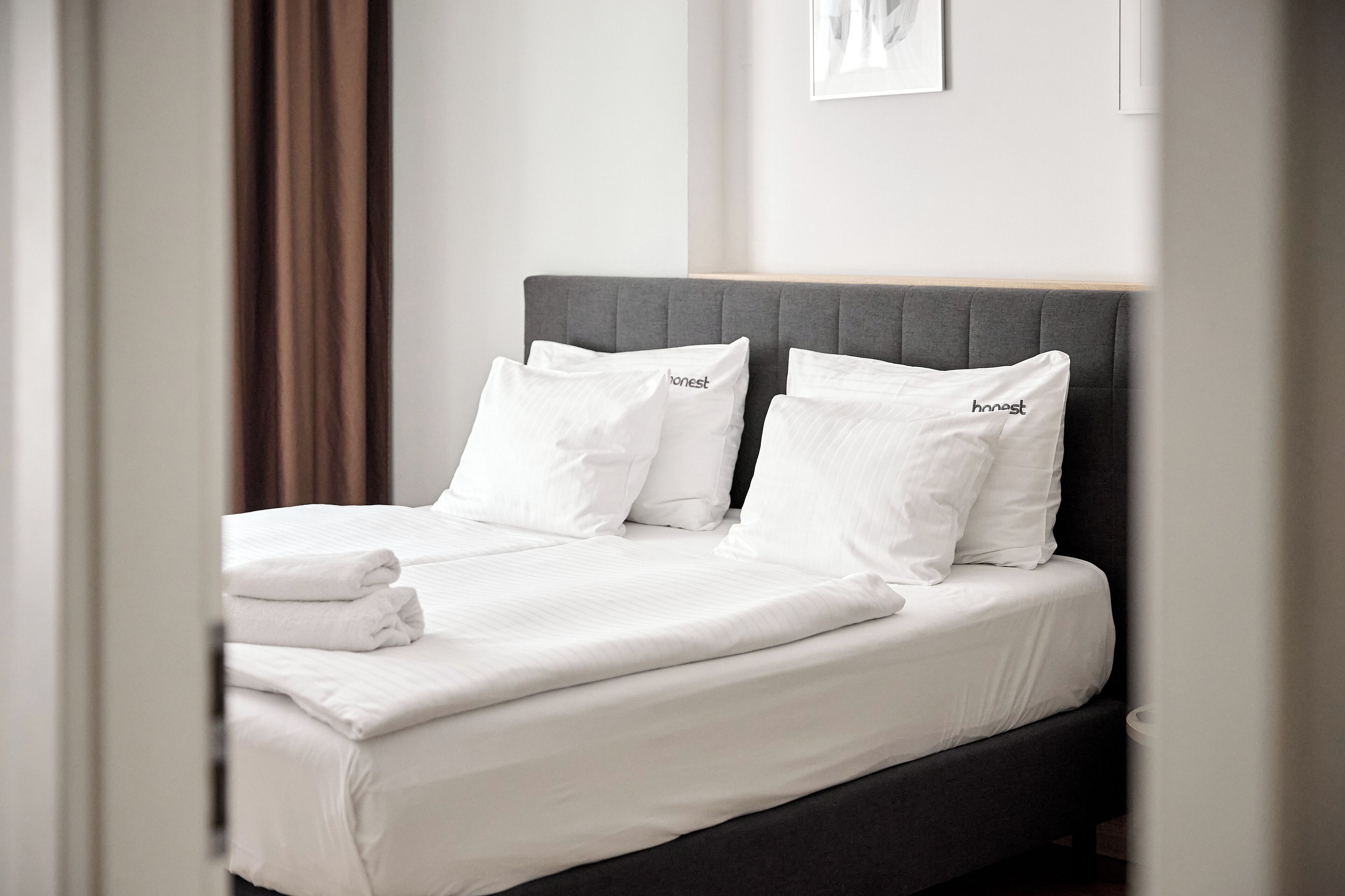 A neatly made bed with white bedding and pillows labeled "honest" in a modern hotel room.