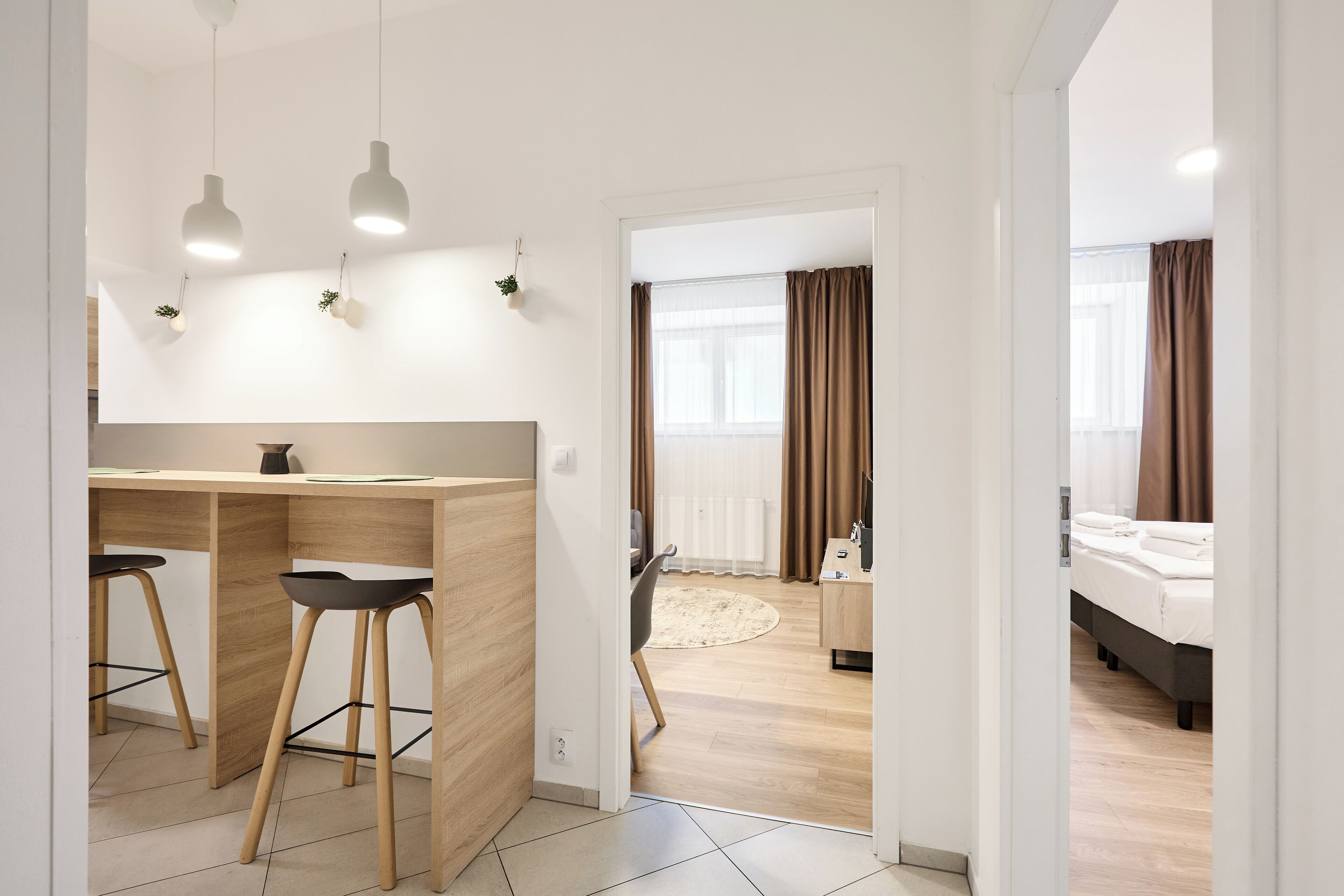 A modern room with a wooden desk, two black stools, a bed, and a large window with curtains.