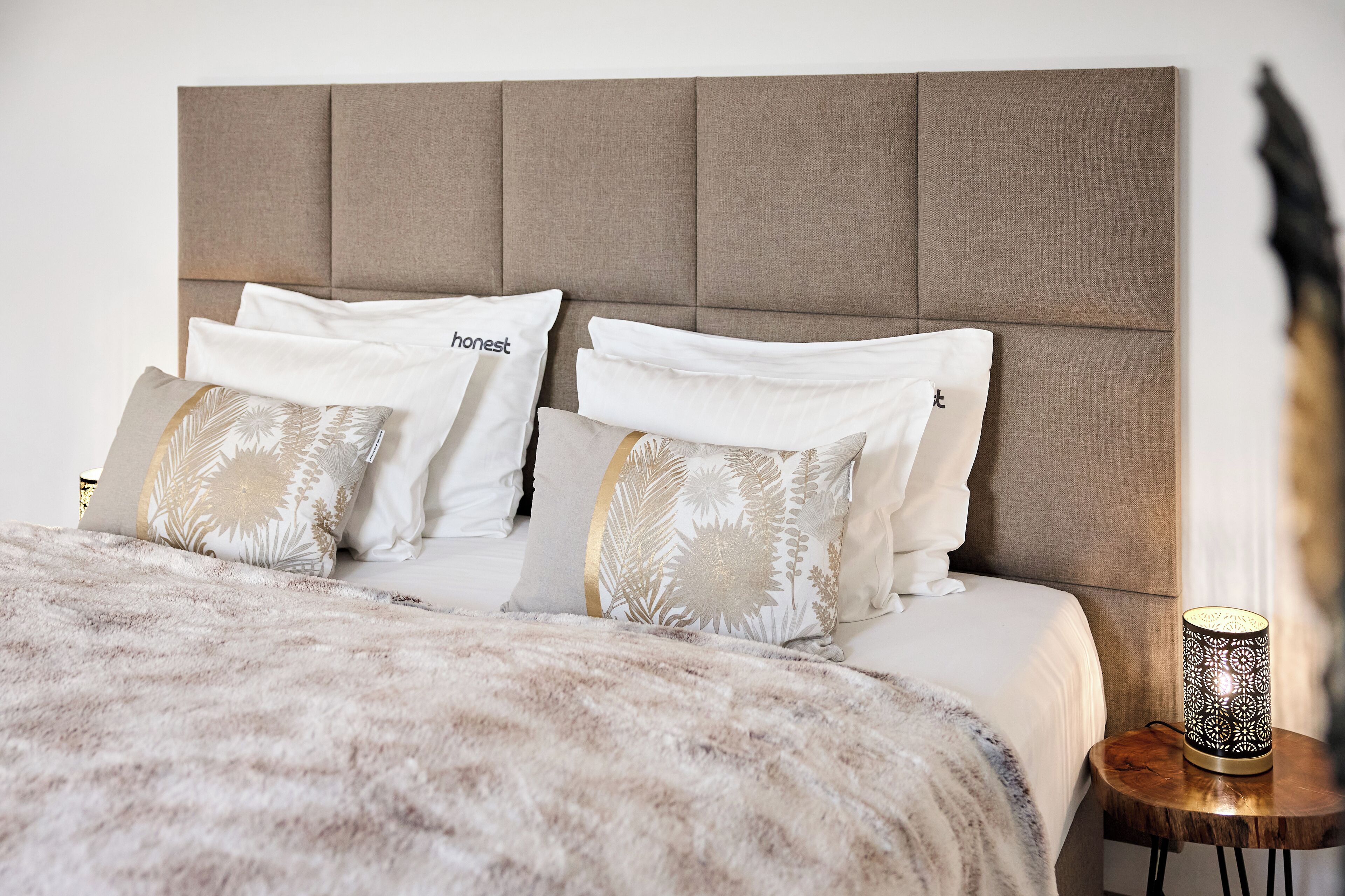 Een opgemaakt bed met een zachte deken, twee kussens met bloemenprint en een nachtkastje met een decoratieve lamp.