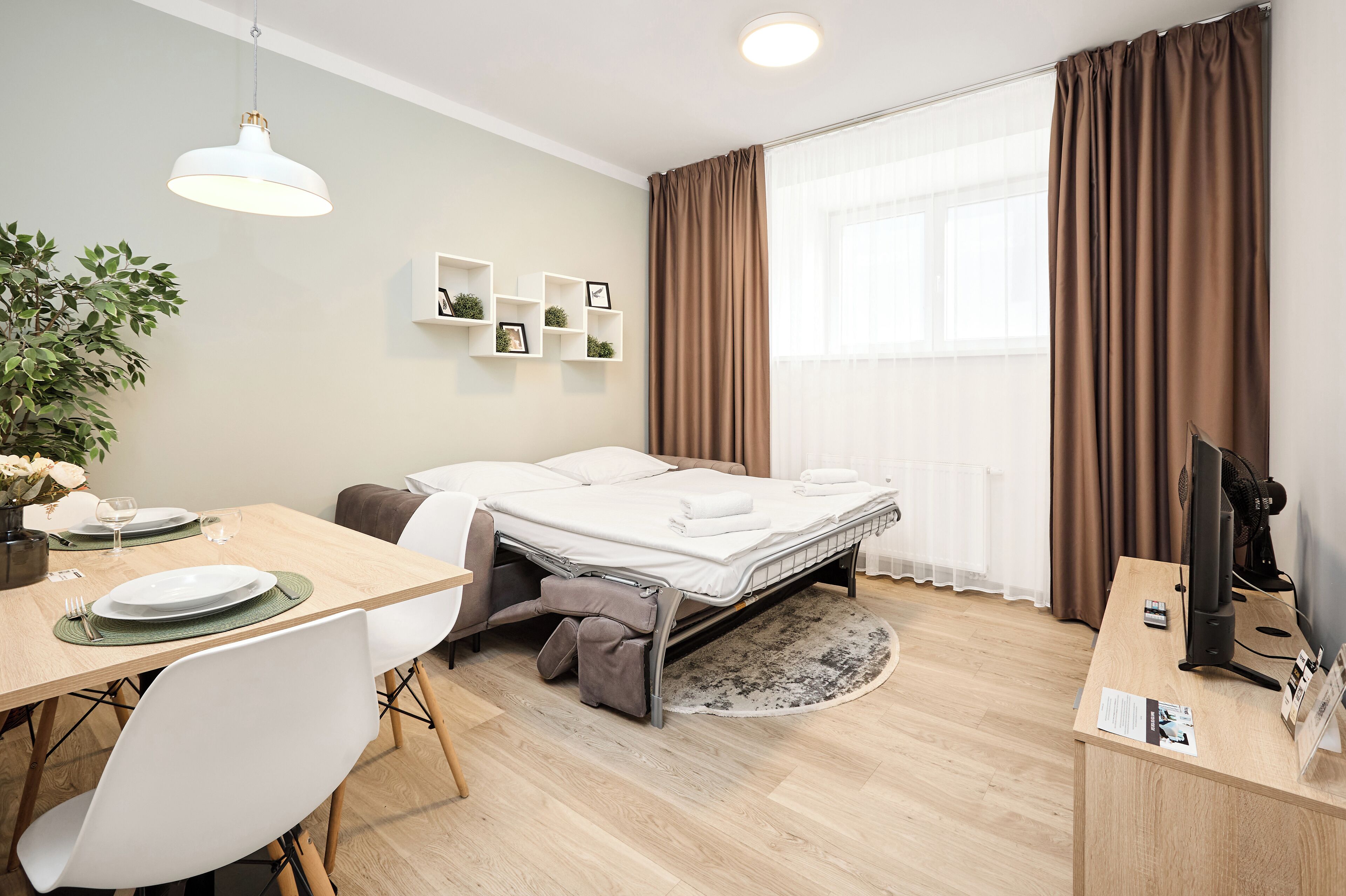 Een kleine hotelkamer met een bed, een bureau, een stoel, een eettafel en een bloempot.