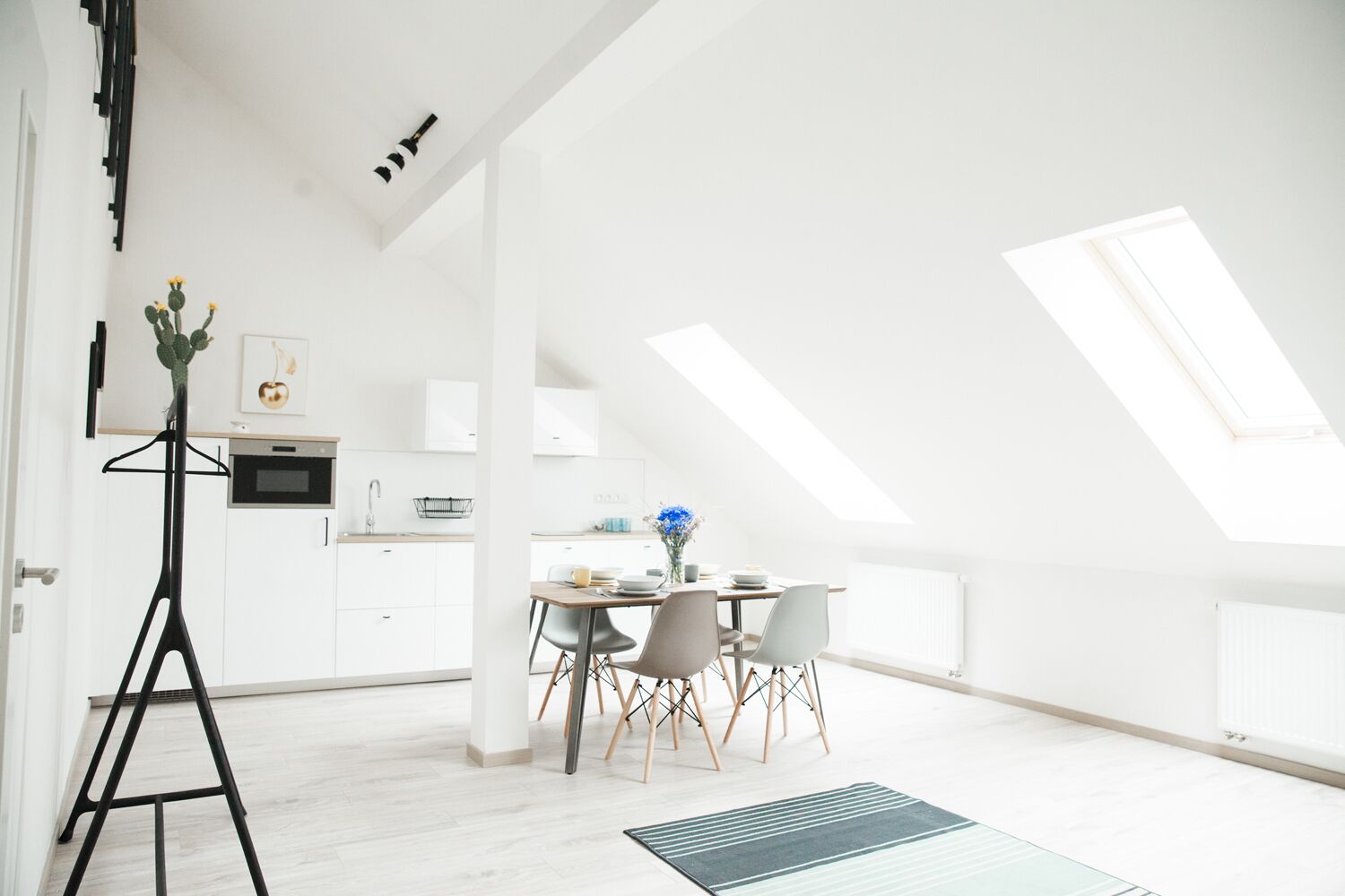 A modern, well-lit room with a dining area, kitchen, and a loft space with skylights.