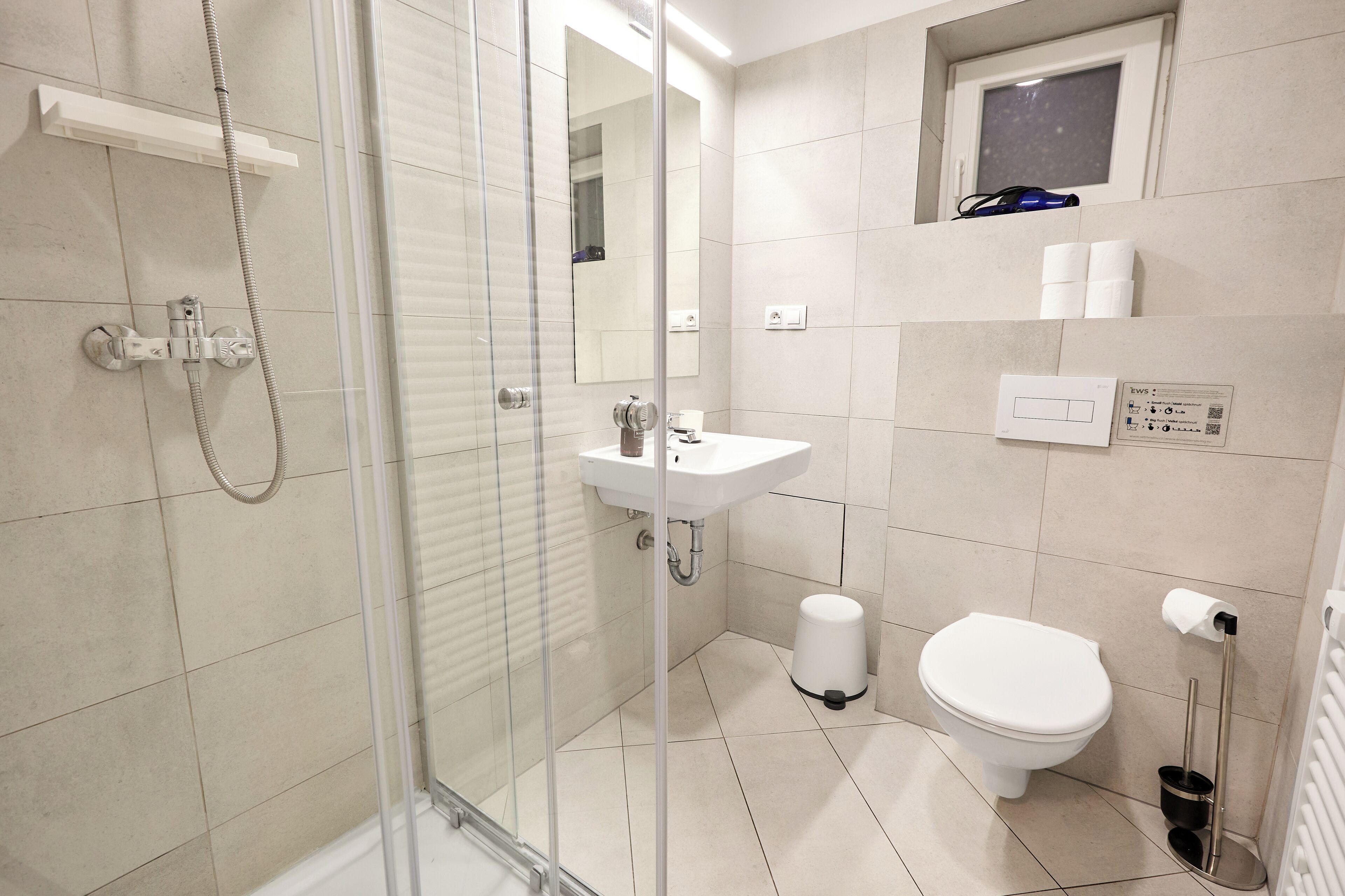 Ein modernes Badezimmer mit Duschkabine aus Glas, Waschbecken, Toilette und kleinem Fenster über der Toilette.