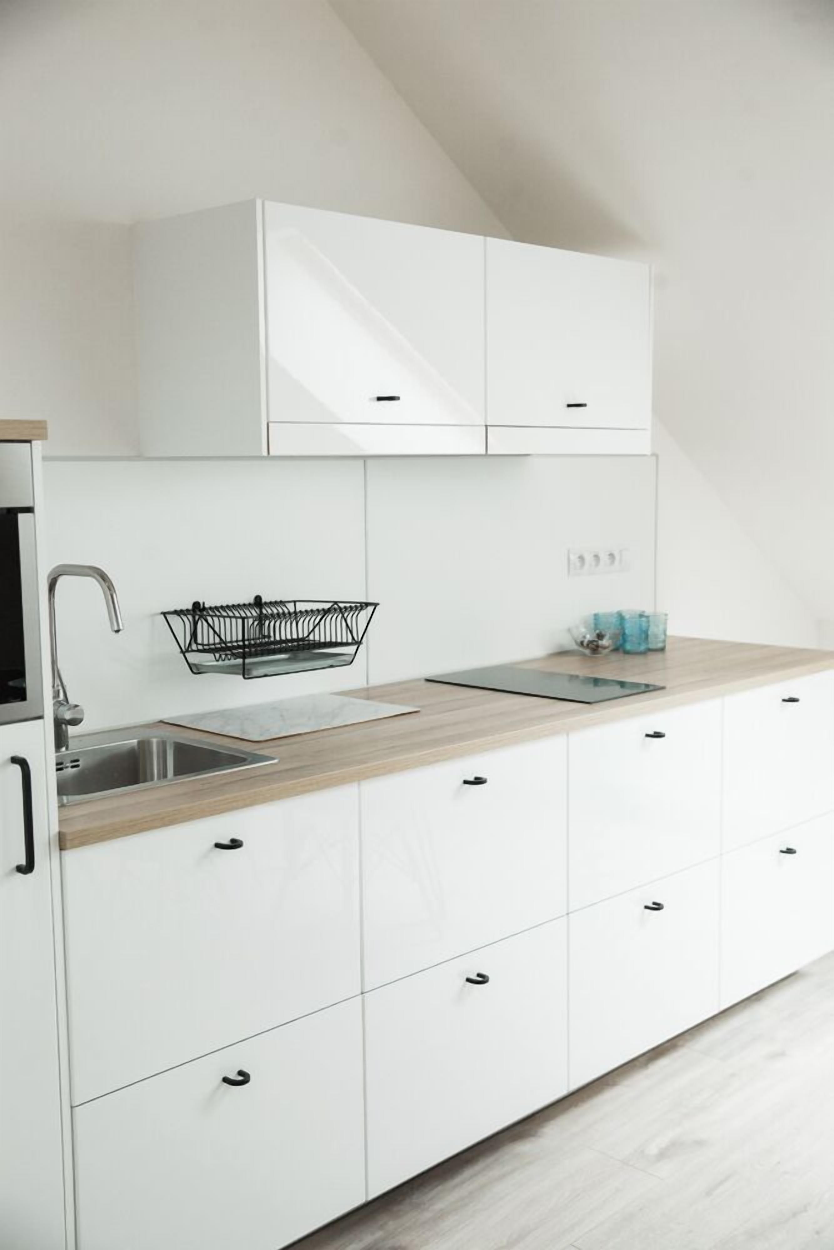 A modern kitchen with white cabinets, a wooden countertop, a built-in sink, and a black dish rack.
