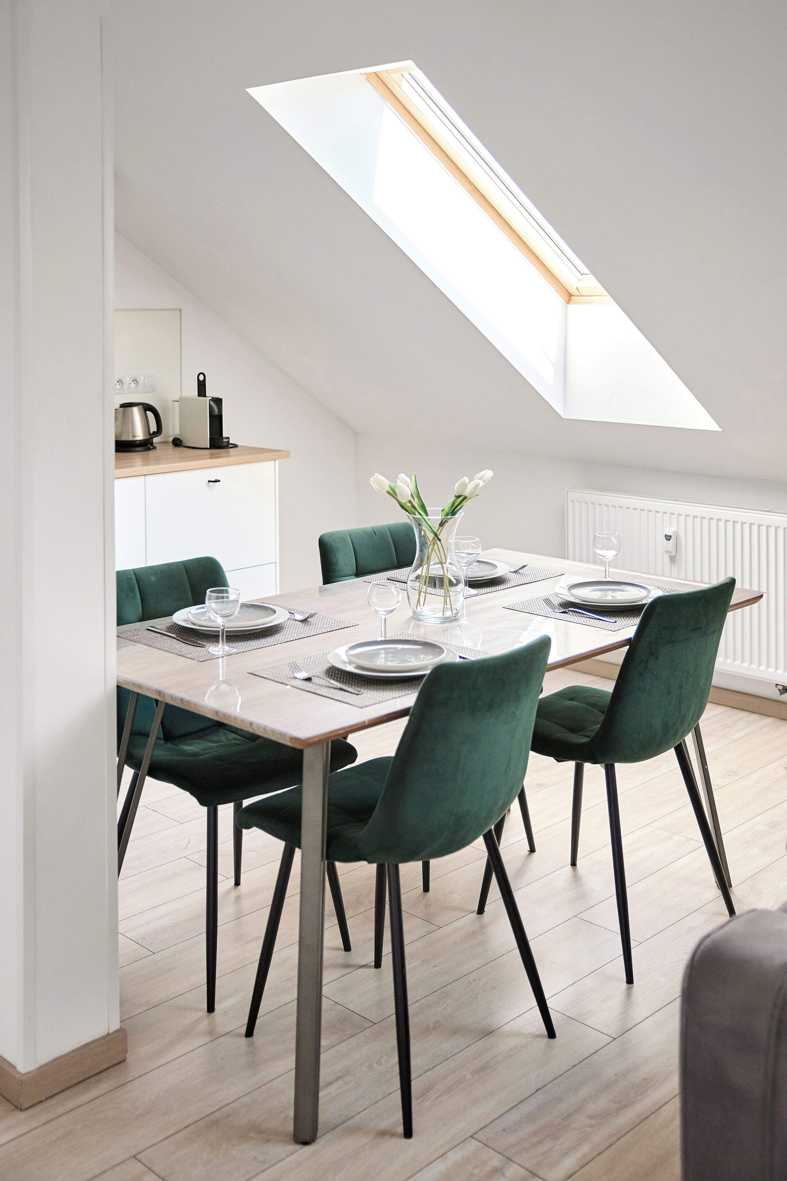 A dining area with a skylight, green chairs, and a table set for four.