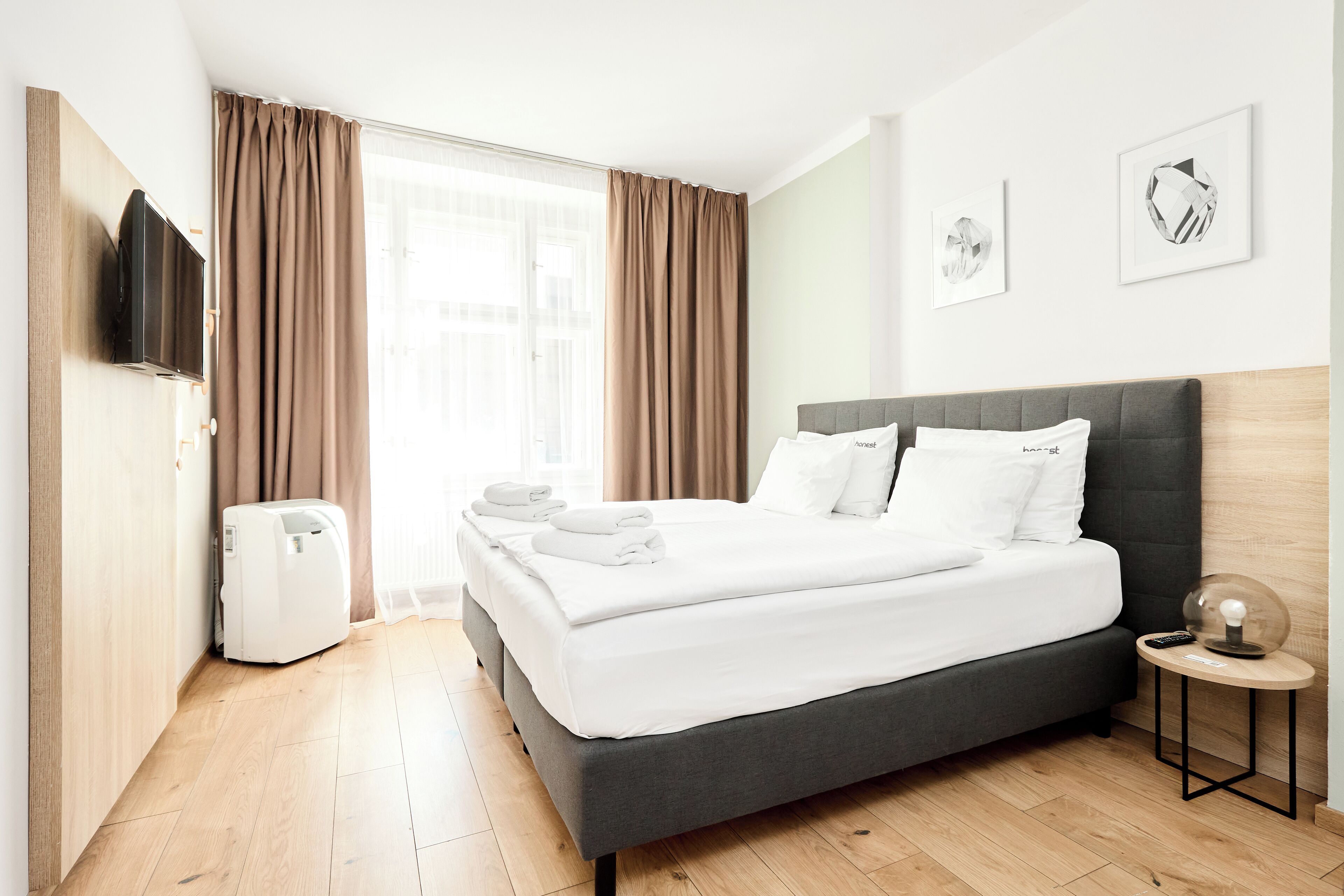 A hotel room with a bed, a TV, a heater, and a small table with a lamp.