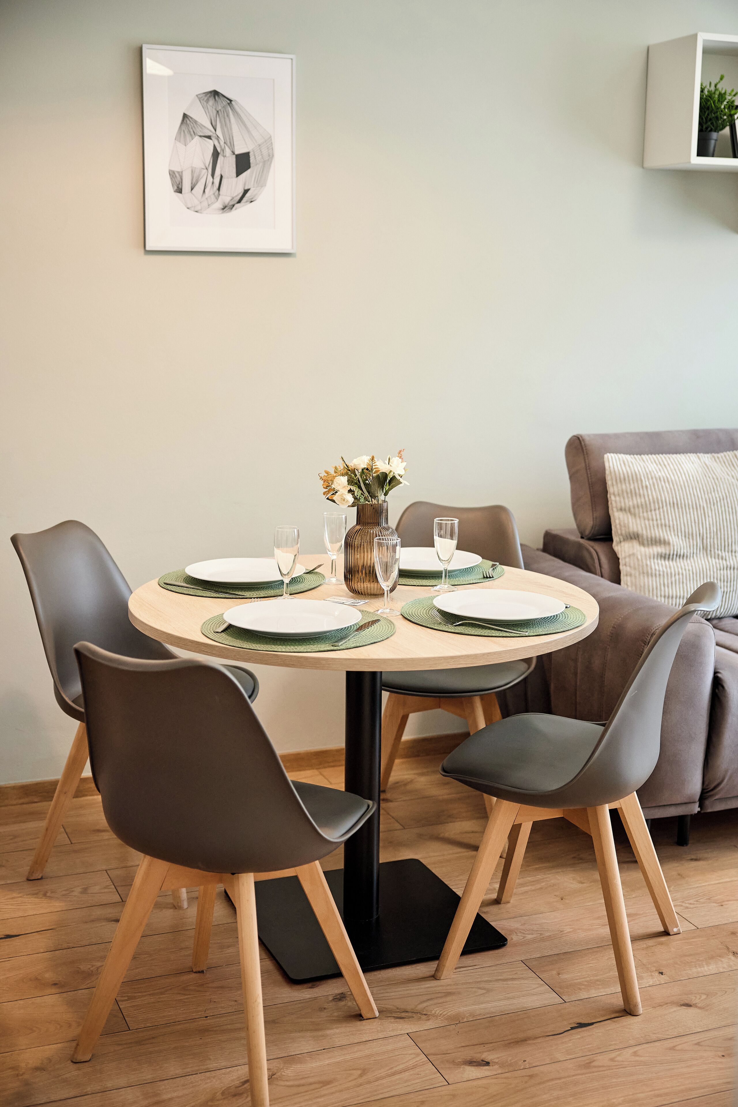 Un coin repas avec une table ronde, quatre chaises, un vase de fleurs et un tableau encadré au mur.