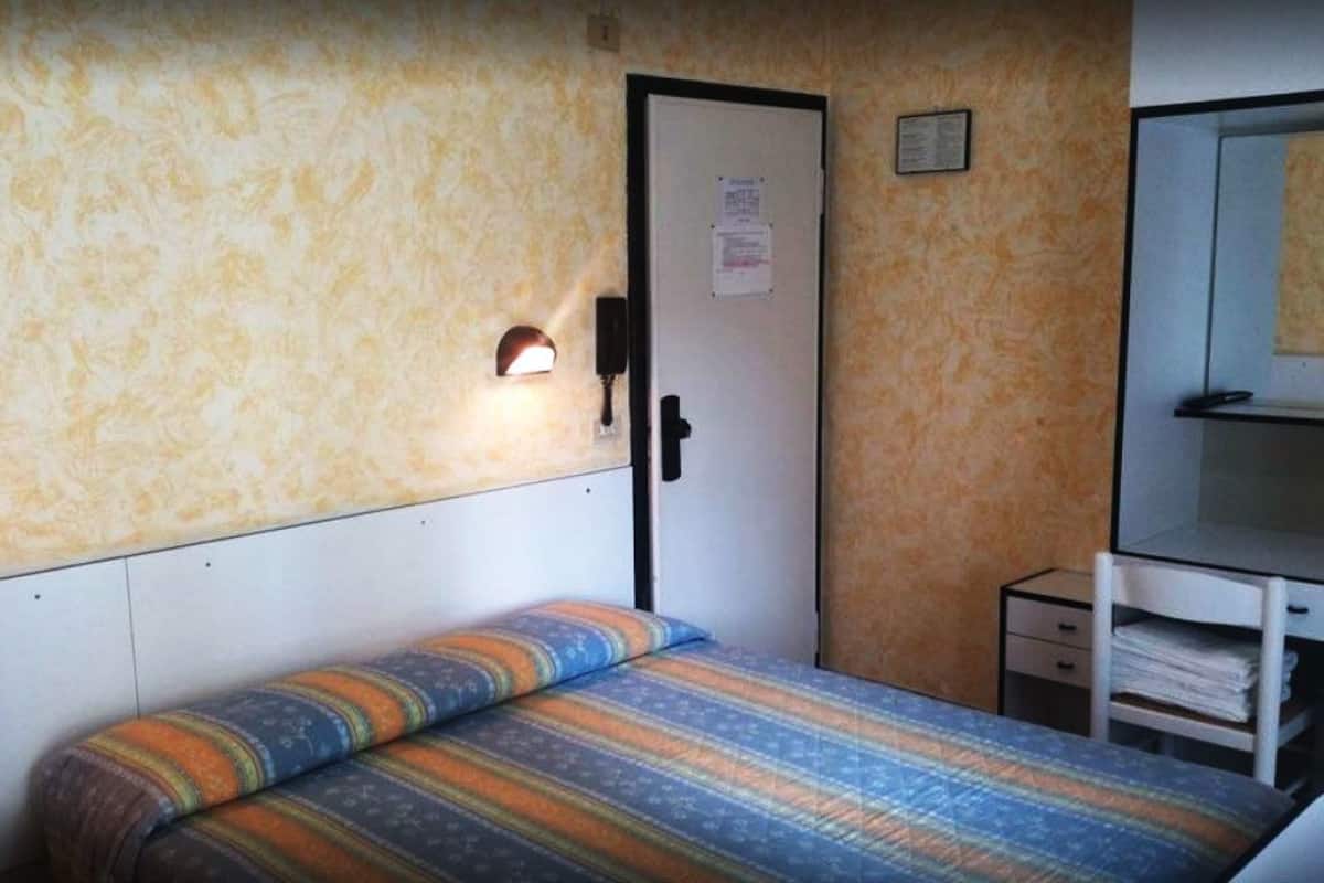 A small room with a bed, a desk, and a door.
