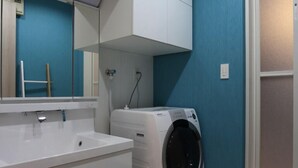 A modern bathroom with a white sink, a built-in washing machine, and a large mirror. - The Neighbors (Osaka)