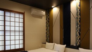 A hotel room with two beds, a sliding shoji screen, an air conditioner, and a decorative mirror. - The Neighbors (Osaka)