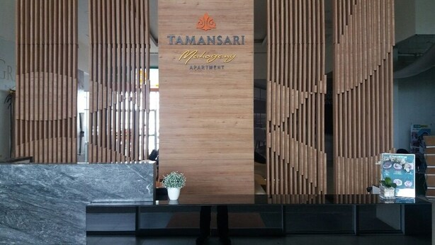Een receptiebalie met een houten paneelwand waarop de naam 'Tamansari Malogany Apartment' staat.