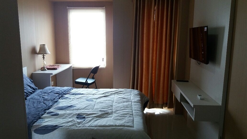 Habitación de hotel con cama, escritorio, silla, televisor y ventana con cortinas.