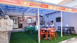 An outdoor dining area with a covered patio, green artificial grass, and a grill station. - Inti's Royal Suite (Abuja)