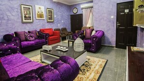 A living room with purple sofas, a red chair, and a coffee table with decorative items. - Inti's Royal Suite (Abuja)