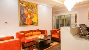 A hotel lobby with orange sofas, a coffee table, a painting on the wall, and a reception desk. - Inti's Royal Suite (Abuja)