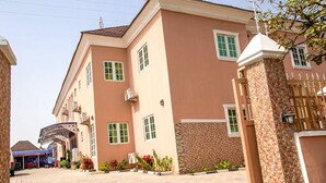 A multi-story residential building with a brick facade, a gated entrance, and a sign indicating 'Plot 287'. - Inti's Royal Suite (Abuja)