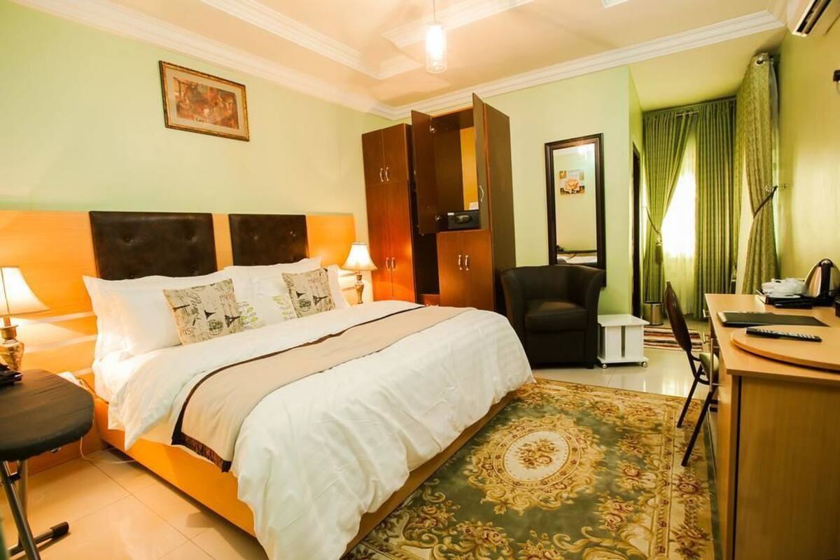 Une chambre d’hôtel avec un lit, des lampes de chevet, un bureau, une chaise, un miroir et un tapis à motifs verts.