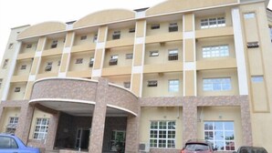 A multi-story building with a curved entrance, multiple balconies, and a parking area in front. - Kanem Suites (Abuja)