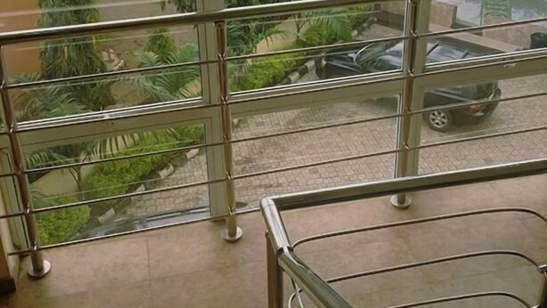 A high-rise building with large windows offering a view of a landscaped area with trees and parked cars. - Kanem Suites (Abuja)
