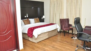 A hotel room with a large bed, a desk with a chair, and a wardrobe. - Kanem Suites (Abuja)