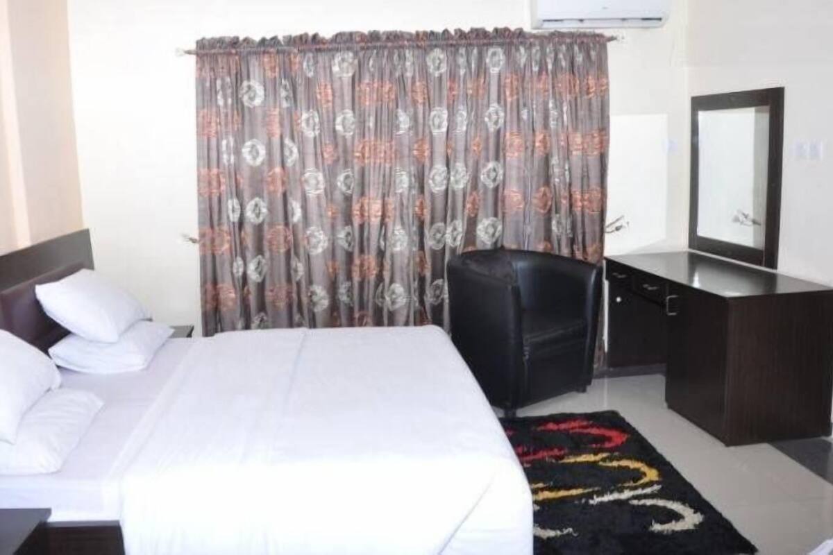 A hotel room with a bed, a desk, a chair, and a mirror.