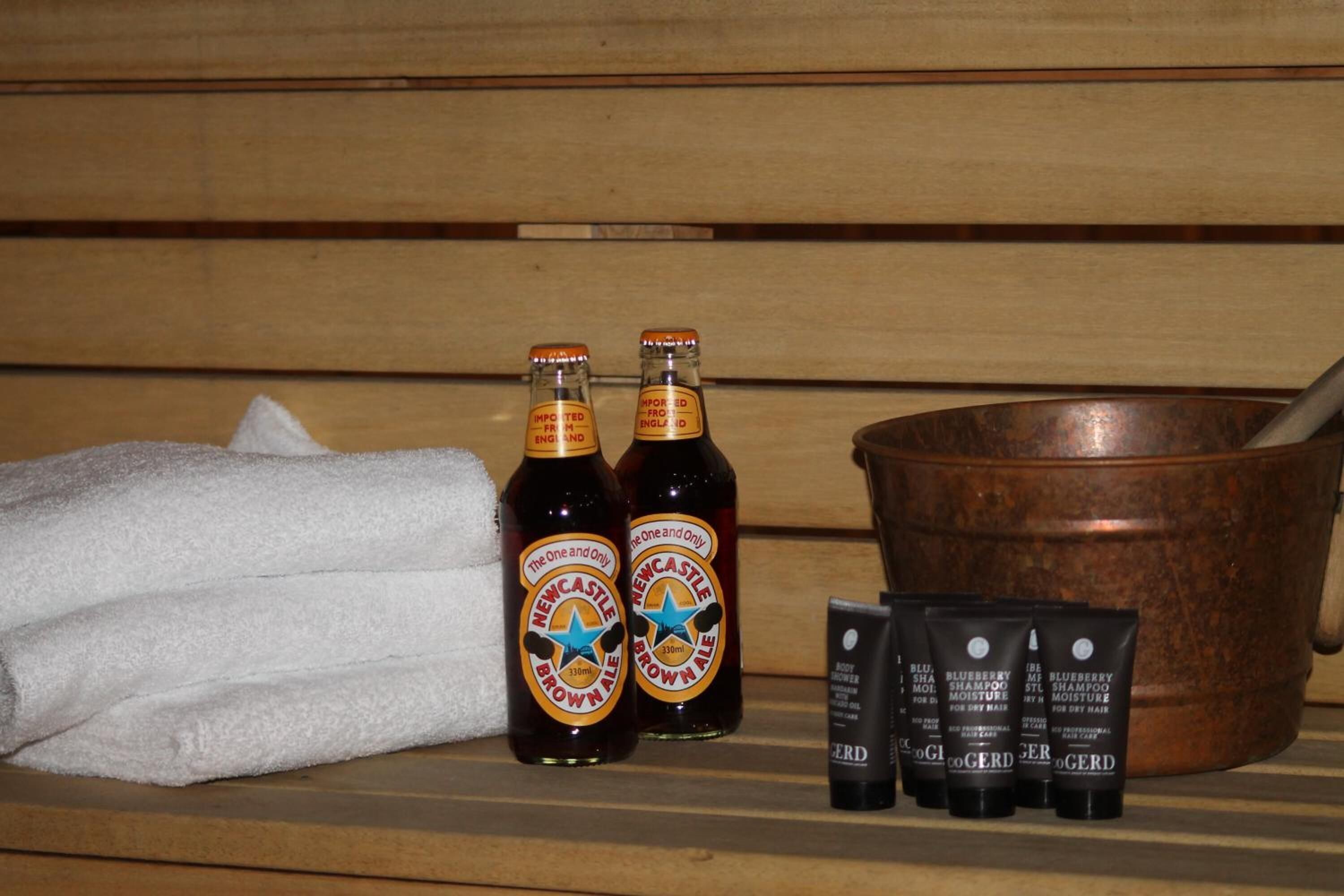 A wooden bench with two bottles of Newcastle Brown Ale, a copper bucket, and four tubes of CoGerD hair products.