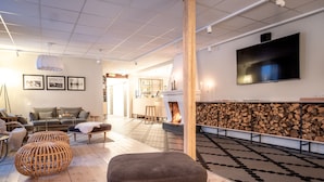 A modern living room with a fireplace, a television mounted on the wall, and a cozy seating area with a sofa and ottoman. - Hotel Akerlund (Jokkmokk)