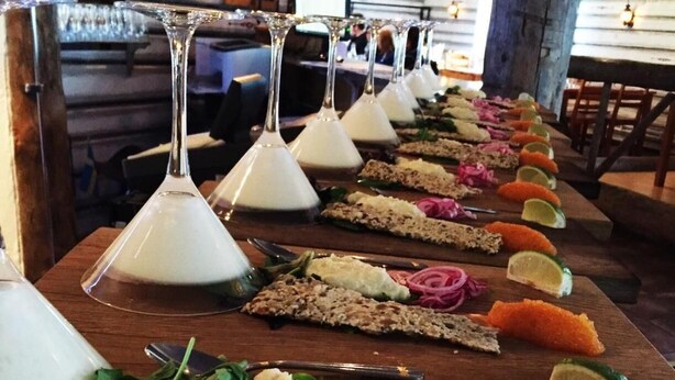 A long wooden table with various food items and glasses of white liquid, likely wine, arranged in a row. - Hotel Akerlund (Jokkmokk)