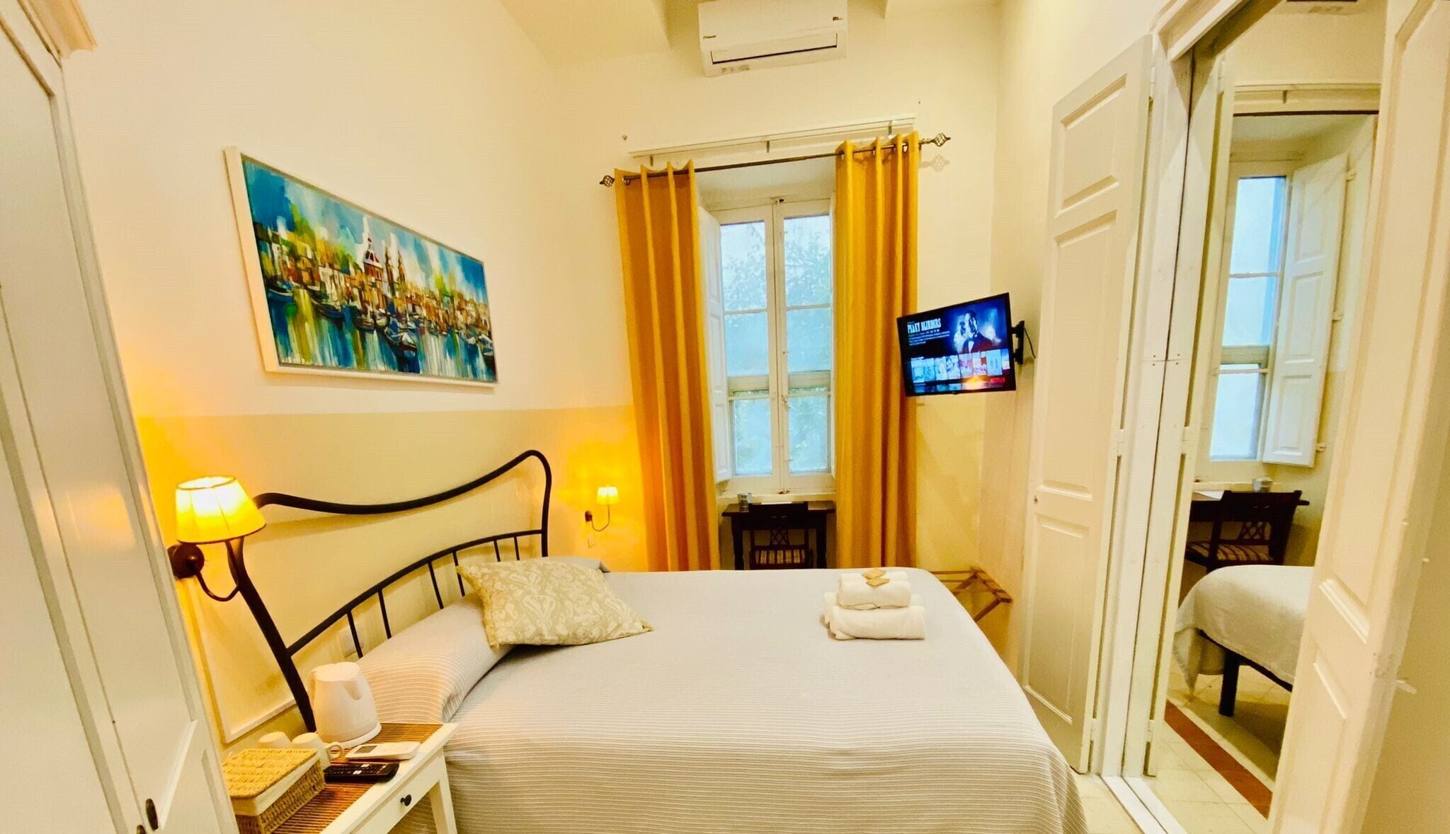Una camera d'albergo con un letto, un quadro, un televisore e una finestra con tende.