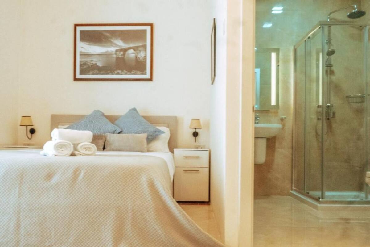 A bedroom with a bed, pillows, a nightstand, a framed picture on the wall, and a glass-enclosed shower area.