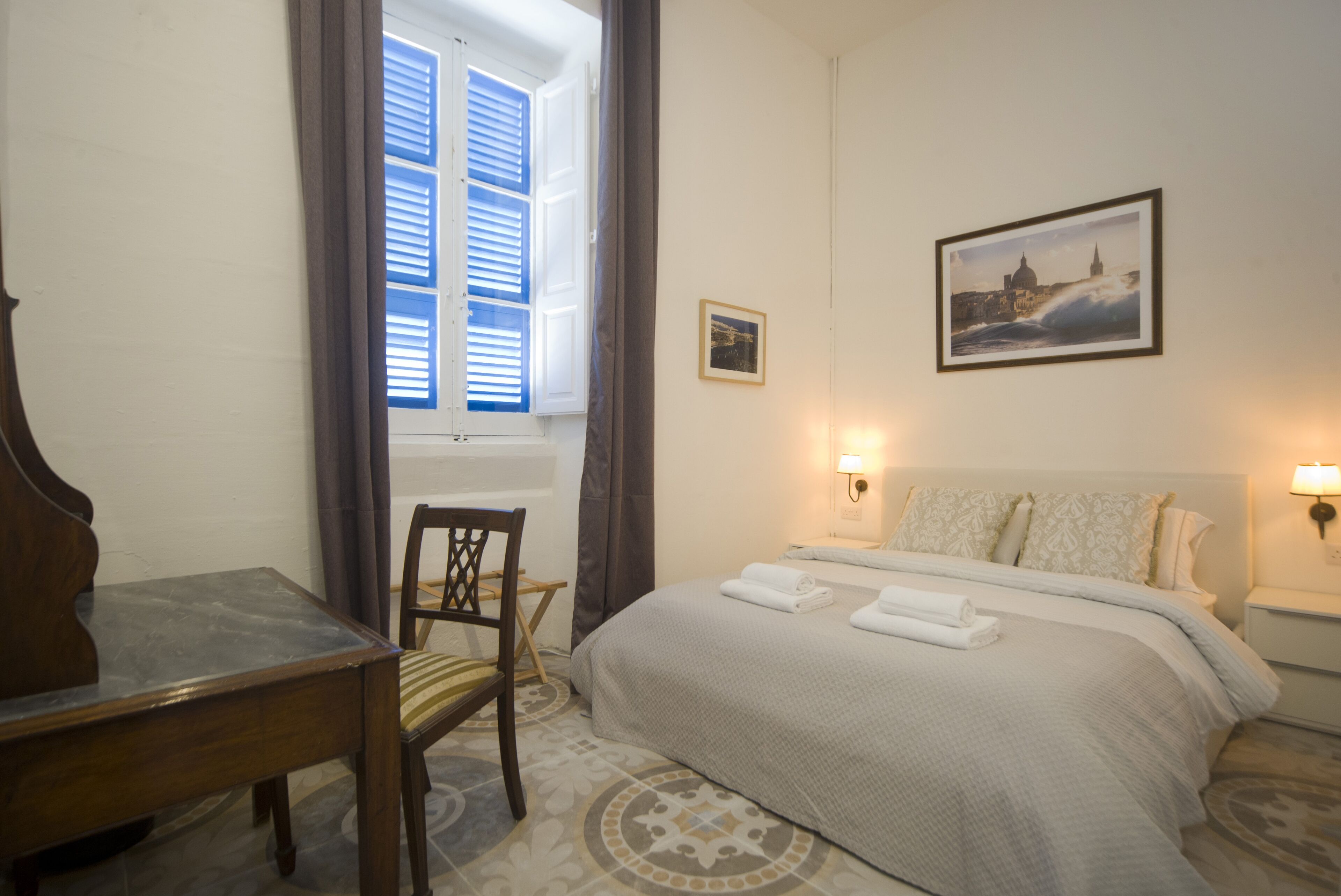 A hotel room with a bed, a desk, a chair, and a window with curtains.