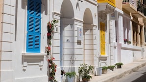 Una hilera de edificios con contraventanas azules y amarillas, fachadas blancas y balcones con plantas en macetas.
