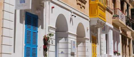 A row of buildings with distinct blue and yellow window shutters, white facades, and balconies with potted plants.