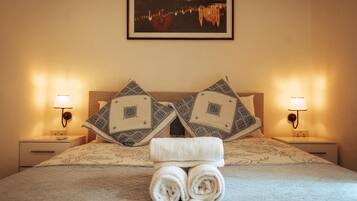 A neatly made bed with two pillows, a folded towel, and a framed picture of a cityscape on the wall.