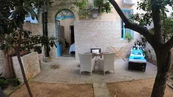 A courtyard with a dining table, chairs, a hammock, and a bed.