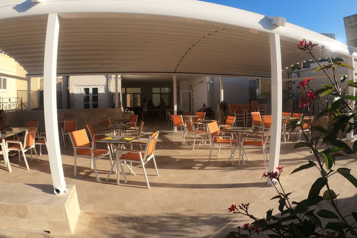 An outdoor cafe area with tables and chairs, a covered seating area, and a view of the surrounding buildings.