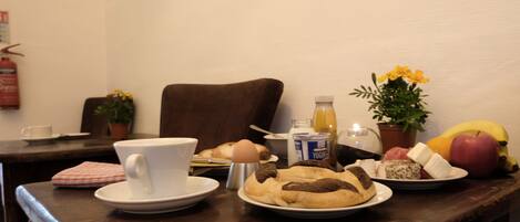 A breakfast table with a cup, eggs, bread, a bottle of juice, a plant, and fruits.
