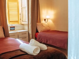 A hotel room with two beds, a nightstand, a lamp, and a window with blinds.