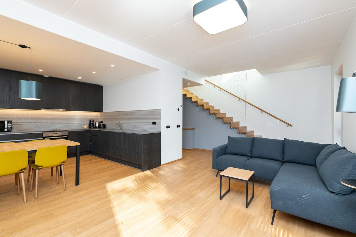 Eine moderne Küche mit Essbereich, einer Treppe und einem Wohnzimmer mit Sofa und Couchtisch.